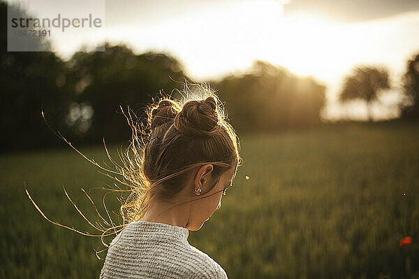 Girl with hair buns in green field at sunset