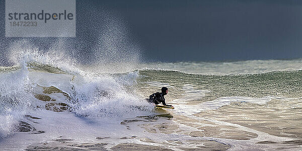 Mann schwimmt im Urlaub mit Surfbrett im welligen Meer
