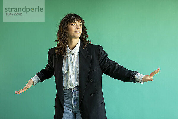 Young woman wearing blazer gesturing against green background
