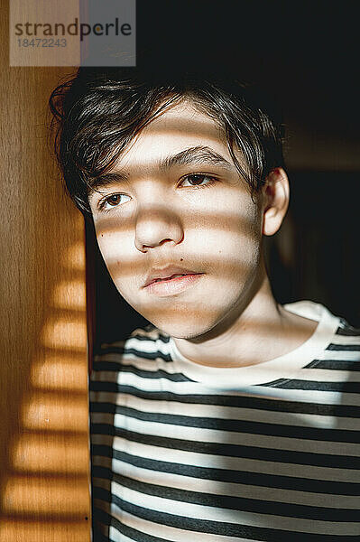 Nachdenklicher Teenager mit Sonnenlicht im Gesicht  der an der Tür steht