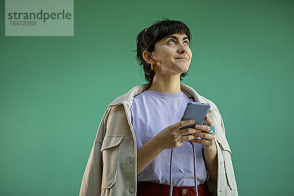 Lächelnde Frau mit Smartphone vor grünem Hintergrund