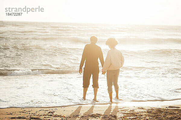 Mann hält Händchen mit Frau  die am Strand steht