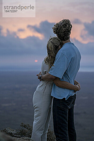 Junges Paar umarmt sich und blickt auf den Sonnenuntergang