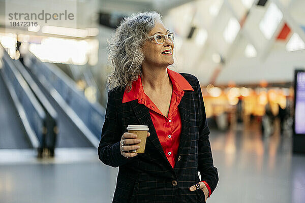 Glückliche reife Geschäftsfrau mit Einwegkaffeetasse an der U-Bahn-Station