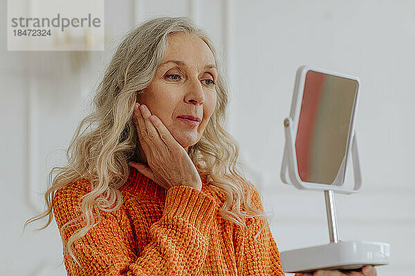 Ältere Frau mit grauen Haaren blickt zu Hause in den Spiegel