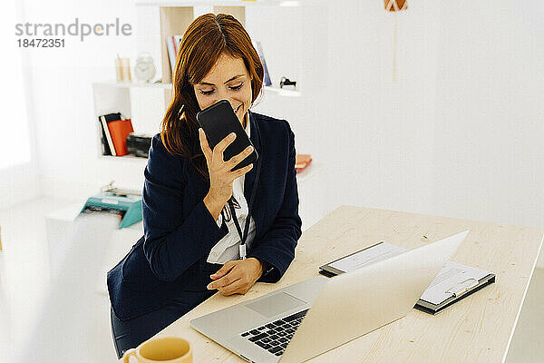 Glückliche Freiberuflerin nutzt Smartphone am Schreibtisch im Heimbüro