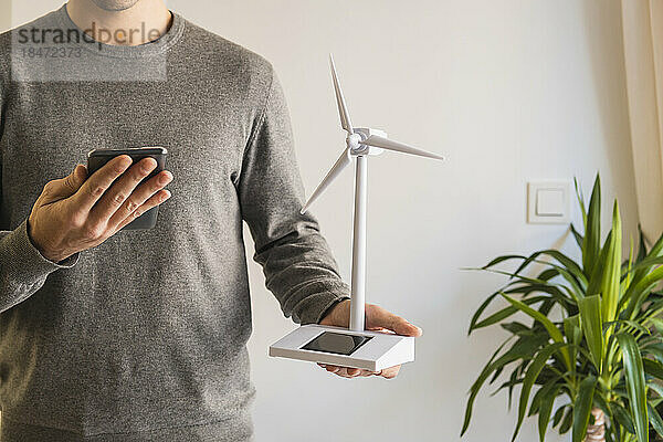 Geschäftsmann mit Windturbinenmodell nutzt Smartphone im Büro