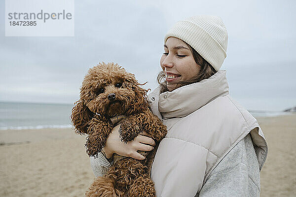 Happy woman holding Maltipoo dog at beach