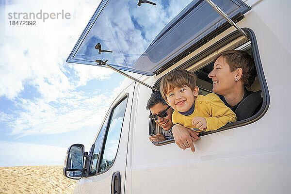 Glücklicher Sohn und Eltern schauen durch das Fenster eines Wohnmobils in die Wüste
