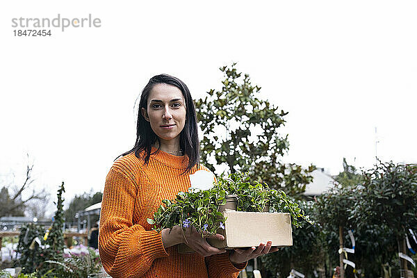 Lächelnde Frau steht mit Topfpflanzen im Gartencenter