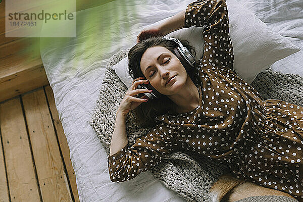 Entspannte Frau  die zu Hause im Bett liegt und Musik über Kopfhörer hört