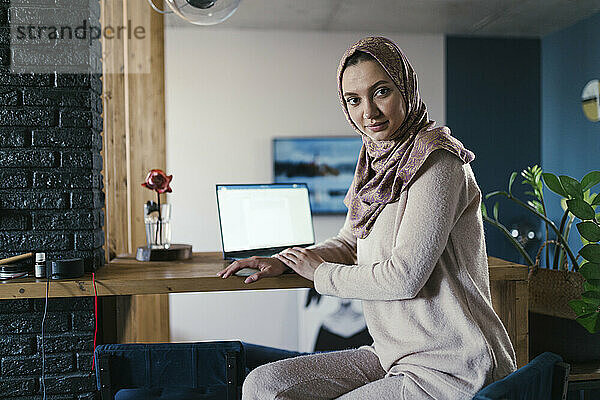 Freiberufler mit Hijab sitzt im Heimbüro am Tisch