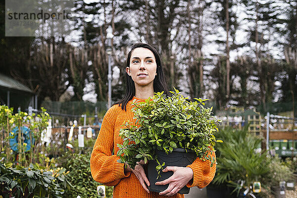 Junge Frau mit Topfpflanze steht im Gartencenter