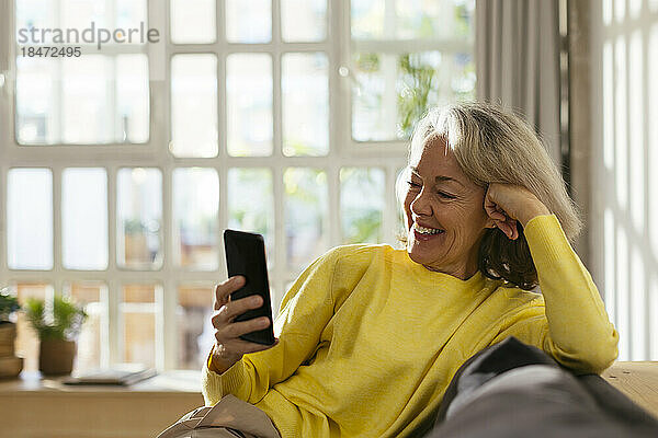 Glückliche reife Frau  die zu Hause auf dem Sofa ihr Mobiltelefon benutzt