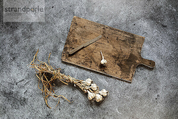 Raw garlic  cutting board and kitchen knife lying on gray surface