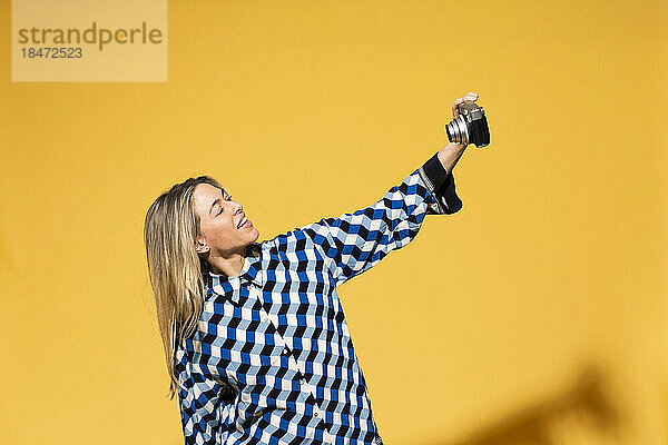 Frau macht Selfie mit der Kamera vor gelbem Hintergrund