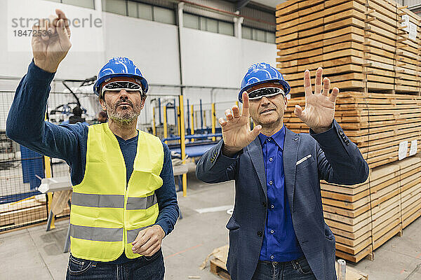 Reifer Ingenieur mit Kollegen  der eine intelligente Brille trägt und in der Fabrik gestikuliert