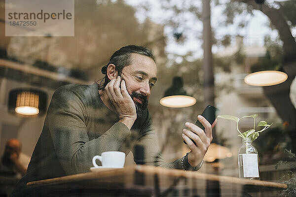 Reifer Mann mit Bart schaut sich im Café einen Film auf dem Smartphone an