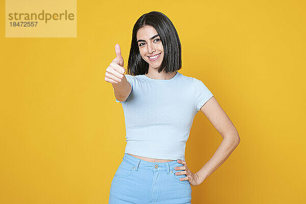 Happy woman showing thumbs up gesture against yellow background