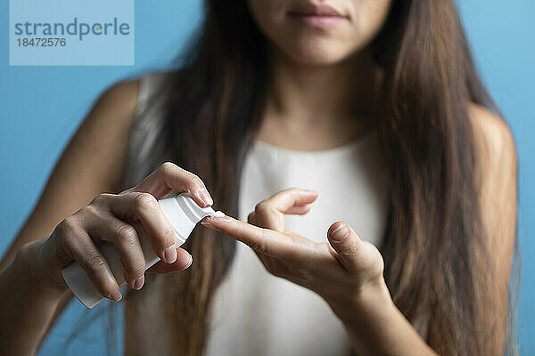 Woman applying cream on finger against blue background