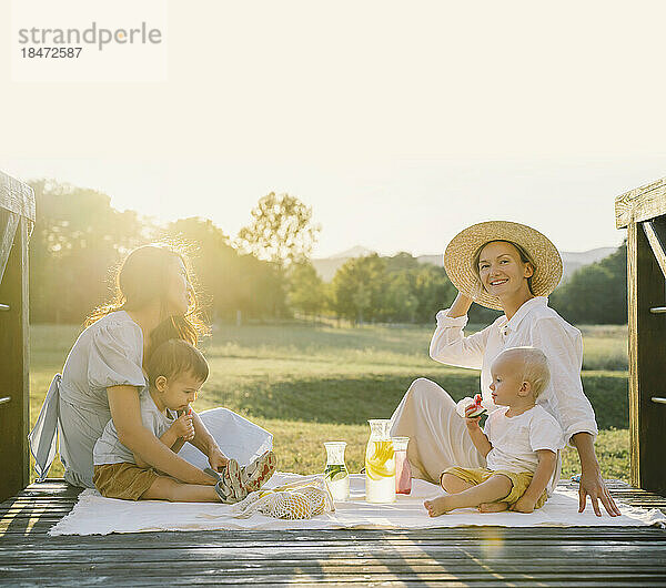 Lächelnde Frauen mit ihren Söhnen verbringen gemeinsame Zeit beim Picknick