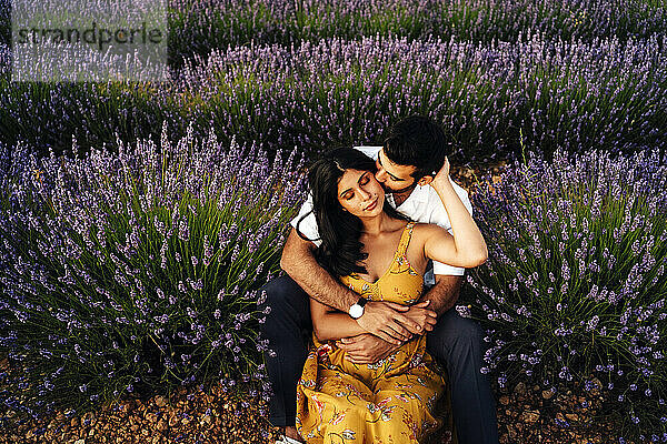 Mann umarmt Frau  die im Lavendelfeld sitzt