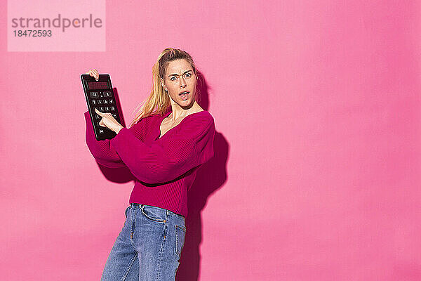 Frau hält großen Taschenrechner vor rosa Hintergrund