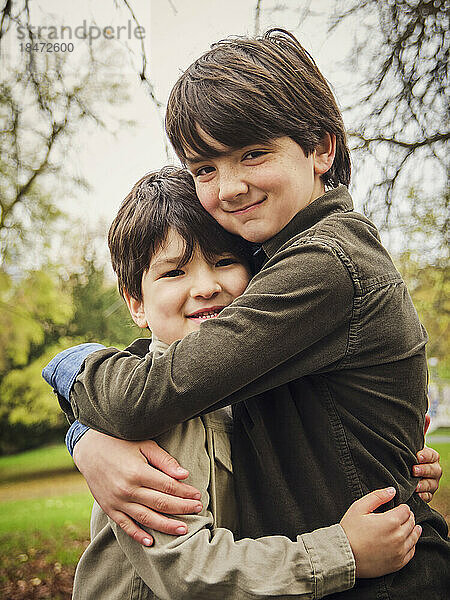 Lächelnder Junge umarmt Bruder im Park