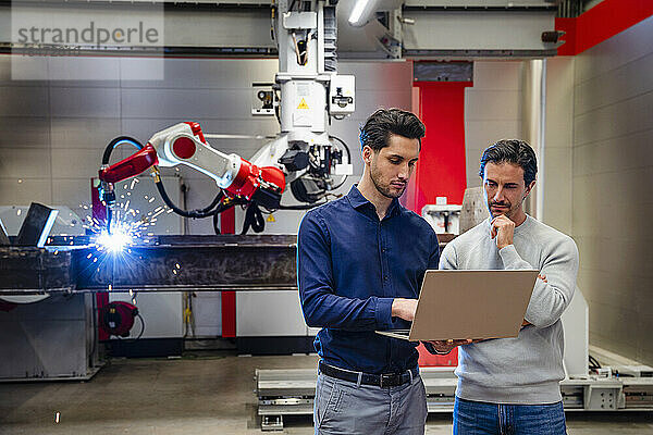 Ingenieur mit der Hand am Kinn steht einem Kollegen mit Laptop in der Industrie zur Seite