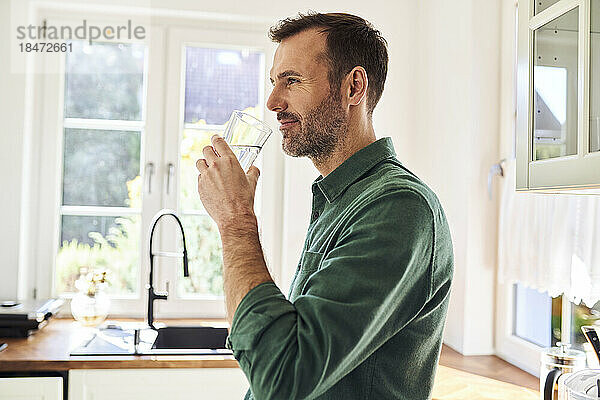 Mann trinkt ein Glas Wasser und steht in der Küche
