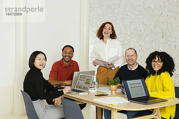 Glückliche Geschäftsleute sitzen am Schreibtisch mit Laptops im Büro