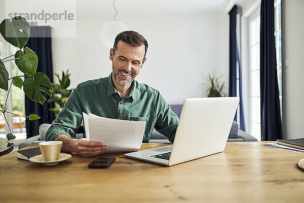 Selbstbewusster Geschäftsmann erledigt Papierkram  sitzt am Tisch und arbeitet von zu Hause aus