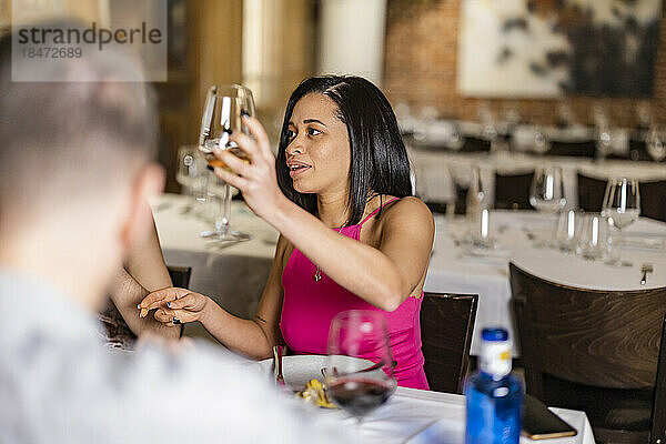 Junge Frau prostet mit Freunden im Restaurant auf Weinglas zu