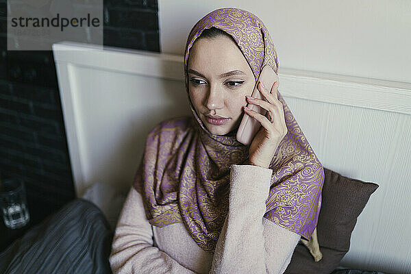 Junge Frau trägt Hijab und telefoniert zu Hause im Bett