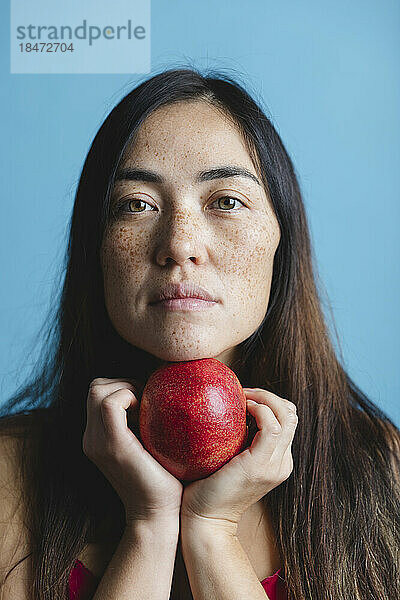 Frau hält Granatapfelfrucht vor blauem Hintergrund