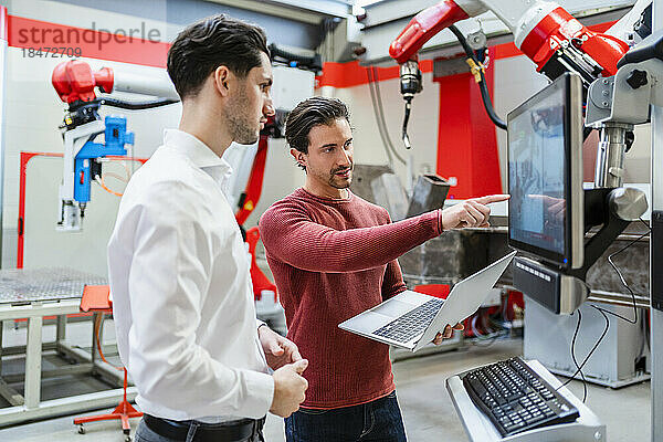 Ingenieur hält Laptop und erklärt Kollegen in Roboterfabrik