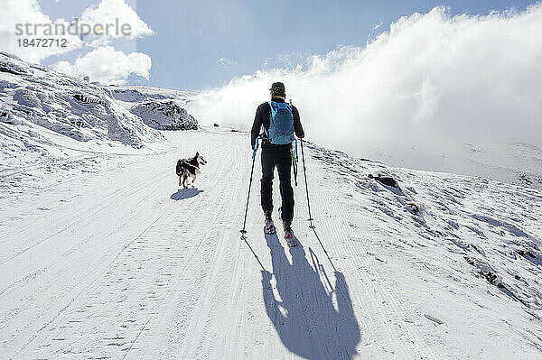 Mann geht an sonnigem Tag mit Hund im Schnee spazieren