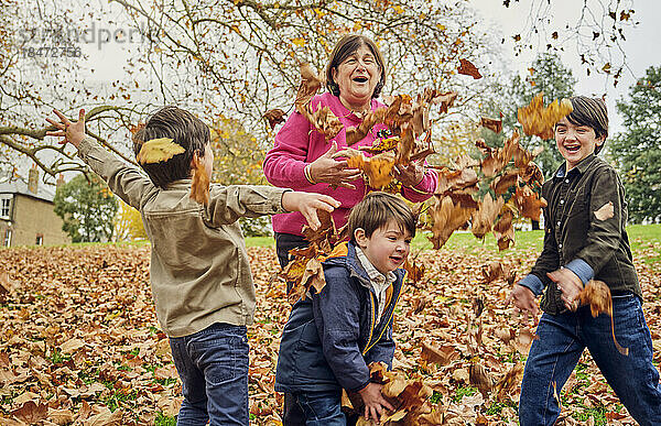 Großmutter spielt mit Enkeln und wirft Herbstblätter in den Park