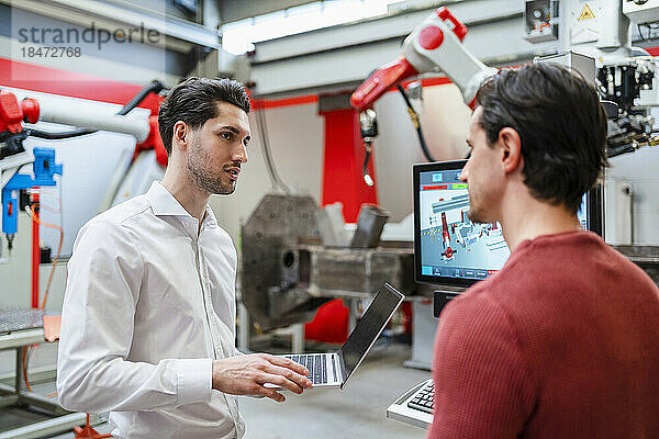 Techniker hält Laptop in der Hand und erklärt Kollegen in der Roboterfabrik