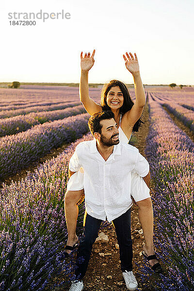 Glückliche Frau genießt Huckepack-Fahrt auf Mann im Lavendelfeld