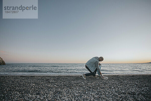 Mann sammelt Müll und reinigt den Strand bei Sonnenuntergang