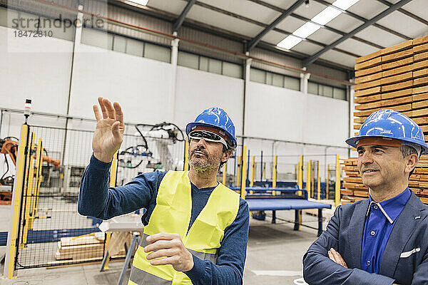 Reifer Ingenieur mit intelligenter Brille gestikuliert von einem Kollegen in der Robotikfabrik