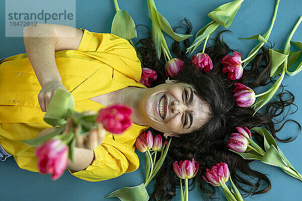 Cheerful woman amidst pink tulips lying on green background