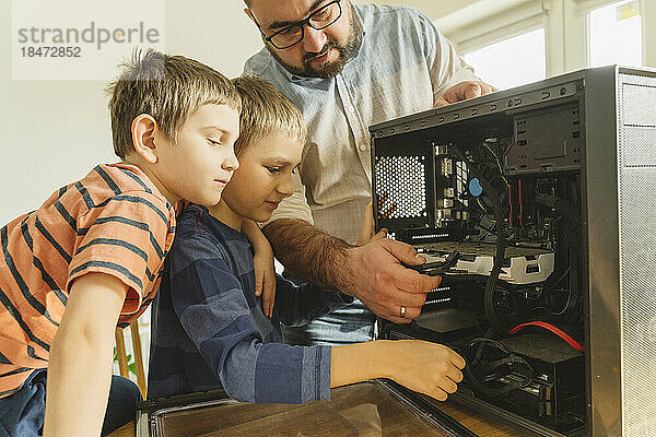 Father teaching sons to repair computer at home