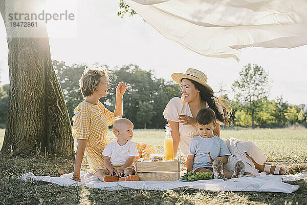 Glückliche Frauen sitzen mit Söhnen auf einer Picknickdecke im Park