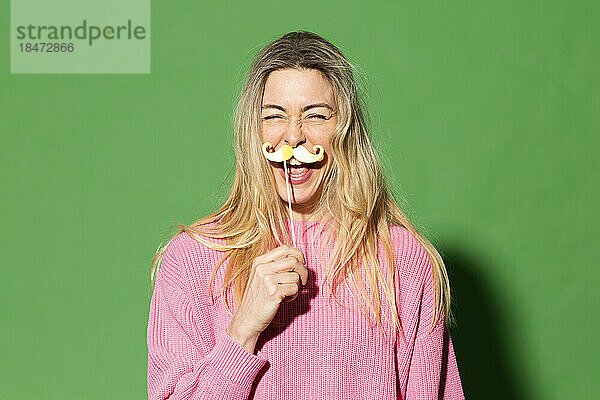 Glückliche Frau imitiert falschen Schnurrbart vor grünem Hintergrund