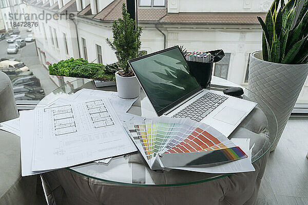 Laptop with documents and color swatches on table at office