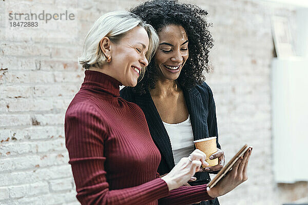 Glückliche Geschäftsfrauen diskutieren über Tablet-PC im Büro