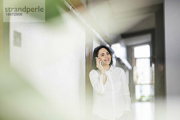 Lächelnde Frau  die an der Wand steht und mit ihrem Mobiltelefon spricht