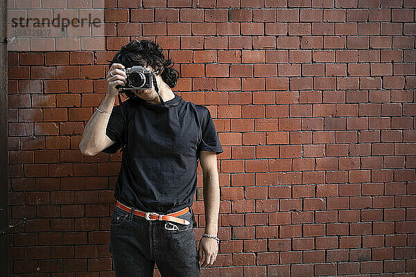 Man photographing through camera in front of brick wall